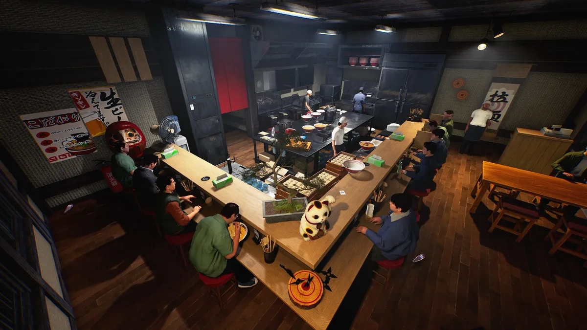A ramen shop interior with a central kitchen and customers seated around the counter.